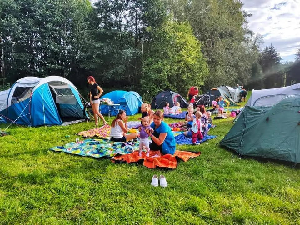 Kempování s dětmi jako letní dovolená s dětmi Maminky a děti sedí na dekách mezi stany v kempu na trávě