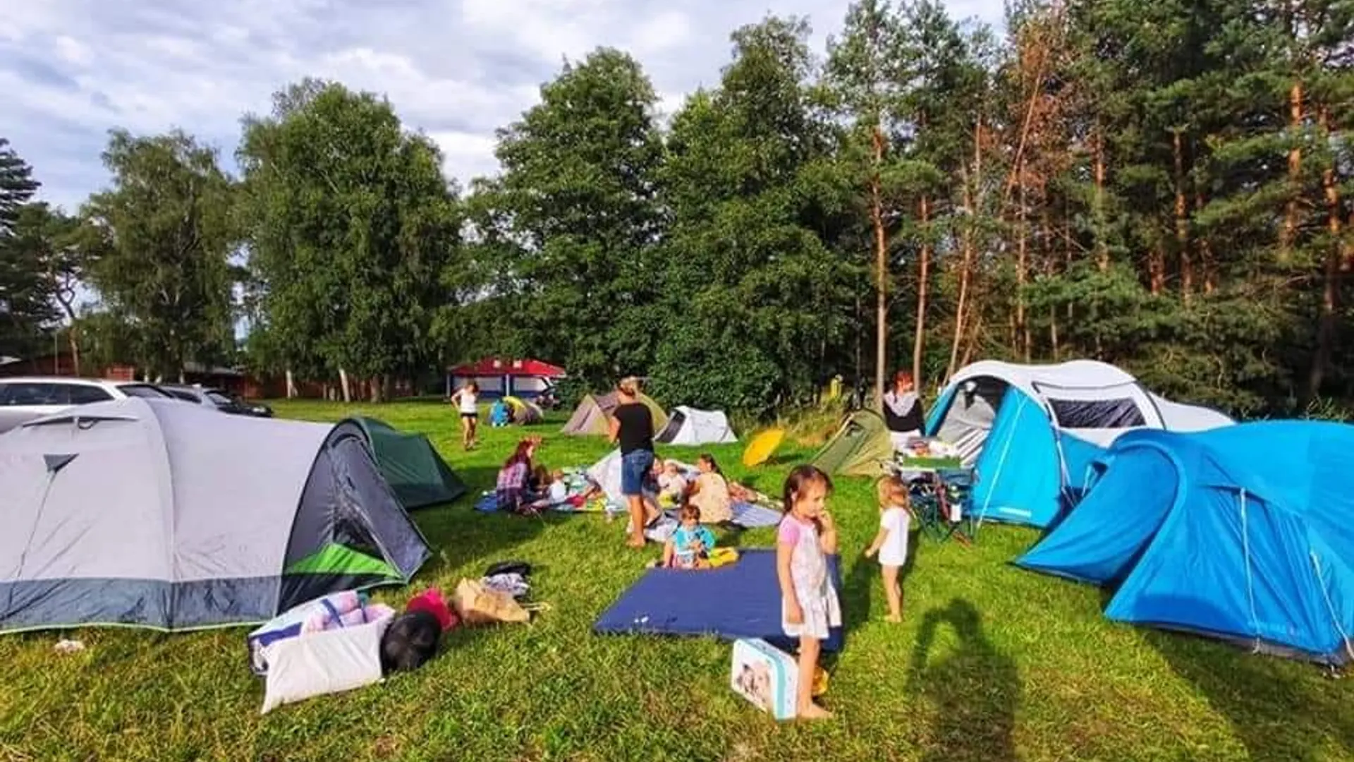 Kempování s malými i většími dětmi Malé i větší děti odpočívají a hrají si na dekách mezi stany v kempu